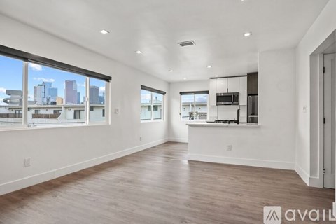 A spacious, empty room with hardwood floors and large windows overlooking a city skyline.
