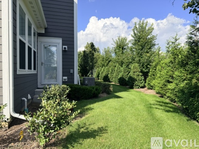 A house with a grey exterior and a white door is surrounded by greenery.
