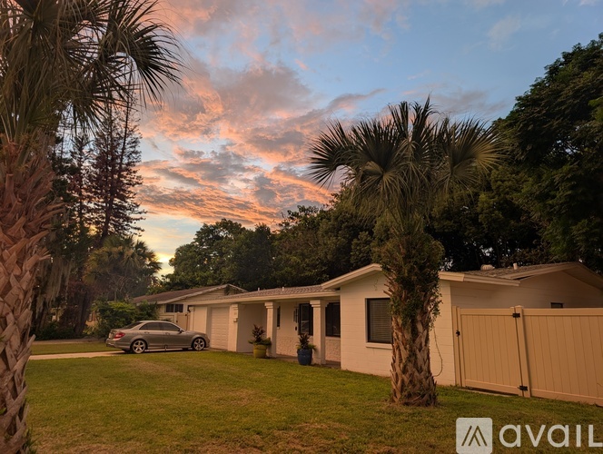 A house with a car parked in front and palm trees in the foreground.