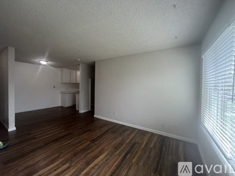 A room with wooden floors and white walls, with a window on the right side.