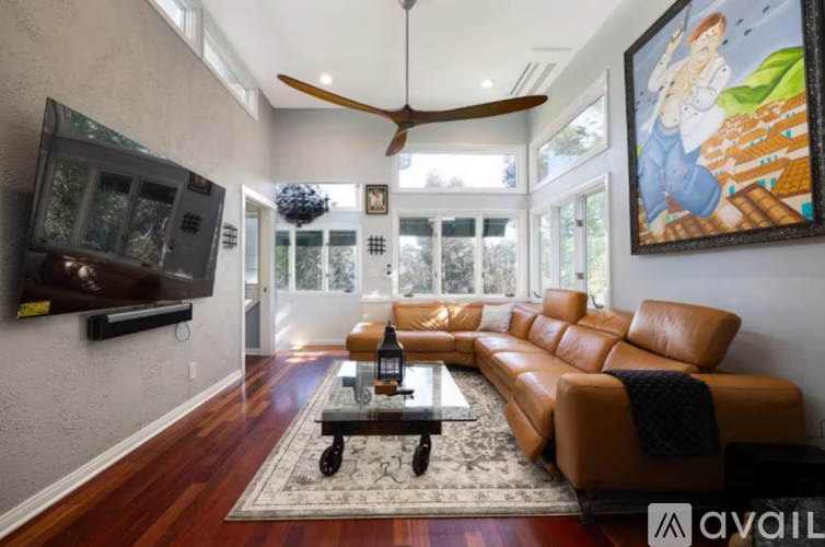 A living room with a brown leather couch and a ceiling fan.