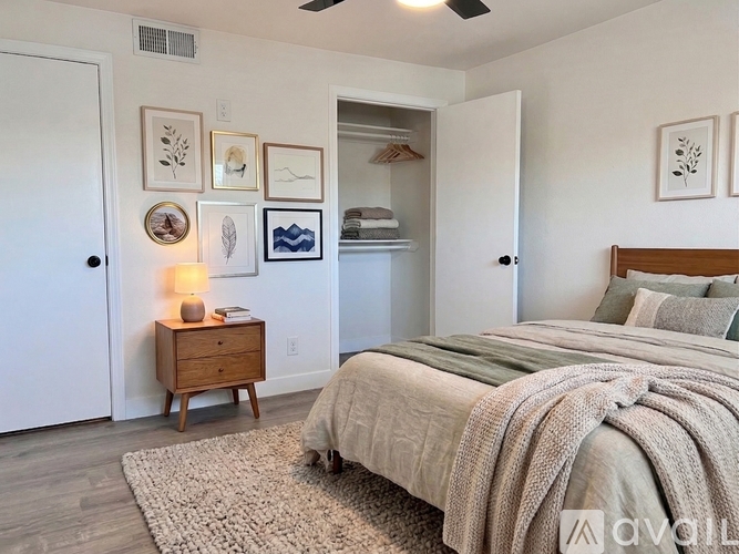 A bedroom with a bed, a nightstand with a lamp, and a wall with framed pictures.