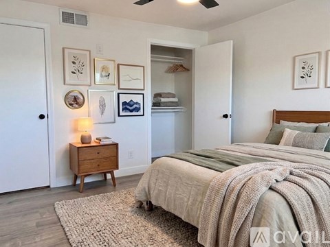 A bedroom with a bed, a nightstand with a lamp, and a wall with framed pictures.