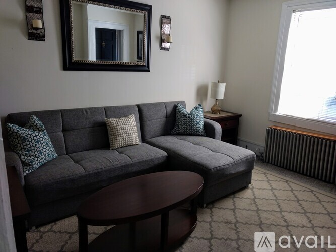 A living room with a grey couch, a brown table, and a mirror on the wall.