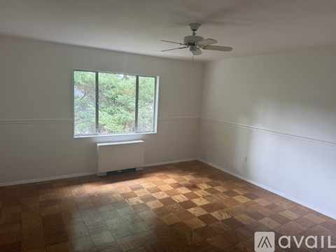 A room with a ceiling fan and a window with a view of trees.