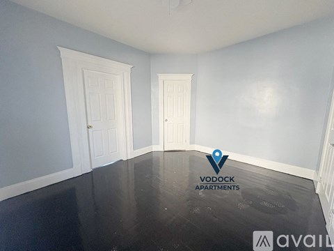 A spacious empty room with two doors and a logo for Vodock Apartments.