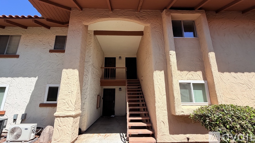 A white stucco house with a brown roof and a staircase leading to the front door.
