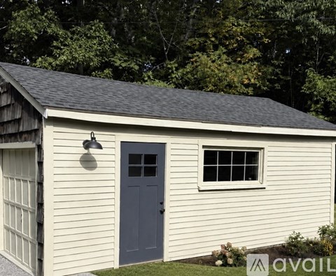 A shed with a grey door and a window is surrounded by greenery.