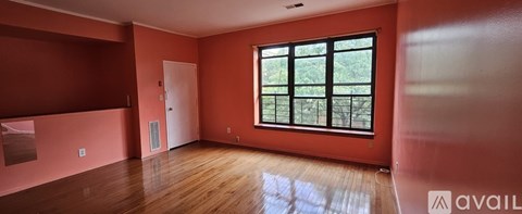A room with a large window and wooden floors is available for rent.