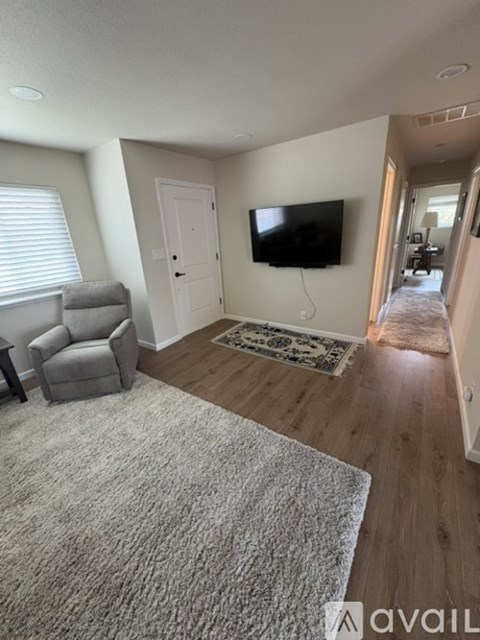 A living room with a grey carpet and a flat screen TV mounted on the wall.