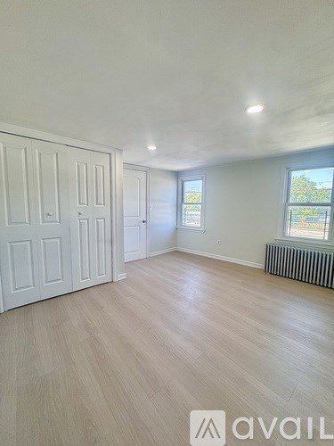 A room with wooden flooring and white walls, featuring a door and a window.