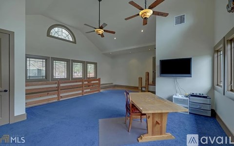 A spacious room with a ceiling fan, a wooden table, and a television.