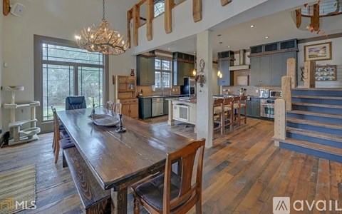A large wooden dining table with chairs is in the center of a spacious kitchen and dining area.