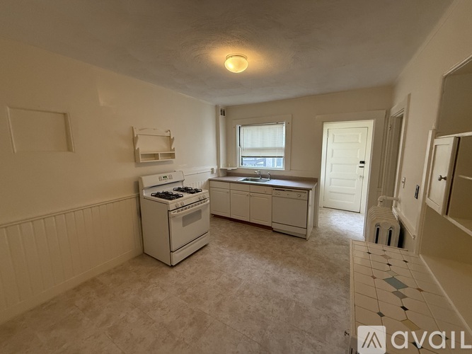 A kitchen with a white stove and cabinets, a window, and a tiled floor.