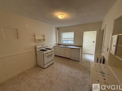 A kitchen with a white stove and cabinets, a window, and a tiled floor.