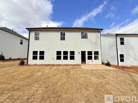 A large white building with a flat roof and multiple windows is surrounded by a dirt lot.