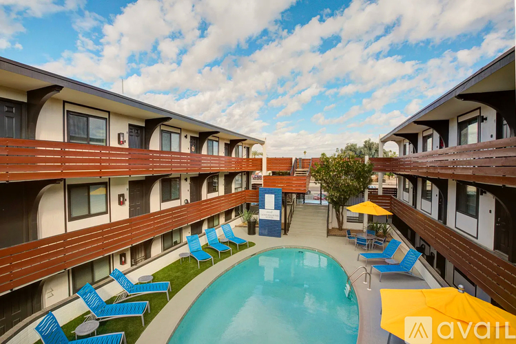 A pool surrounded by lounge chairs and umbrellas is in front of a building.