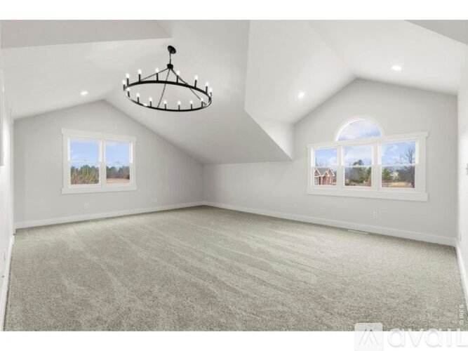 A spacious room with a chandelier, carpeted floor, and two windows.