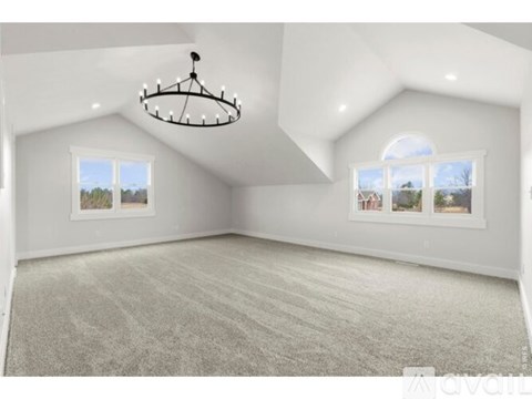 A spacious room with a chandelier, carpeted floor, and two windows.