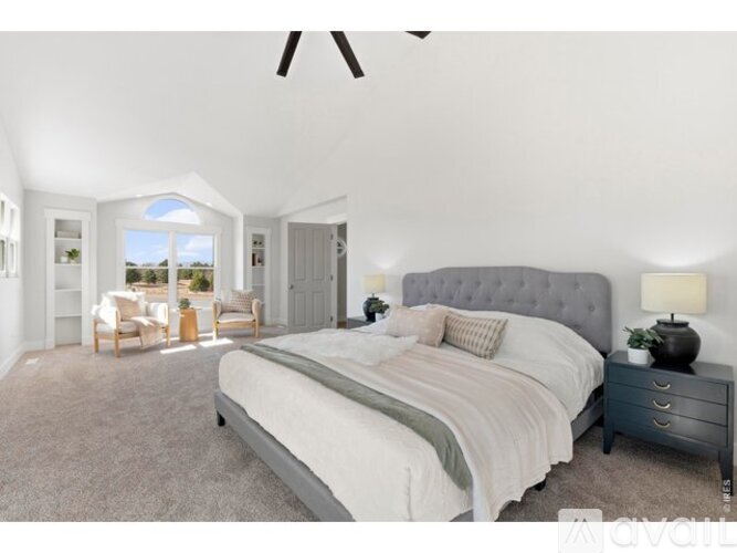 A bedroom with a large bed, a ceiling fan, and a view of the outdoors through a window.