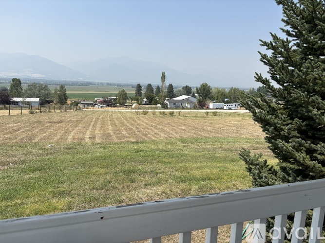 A view from a balcony overlooking a field with a house and trees in the distance.