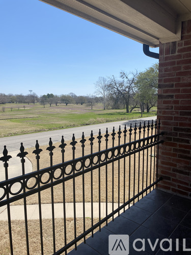 A black iron fence in front of a brick wall with a view of a grassy field.