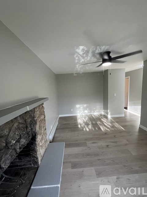 A modern living room with a stone fireplace and a fan on the ceiling.