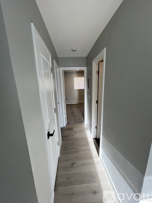 A long, narrow hallway with white doors on the left and a door on the right.