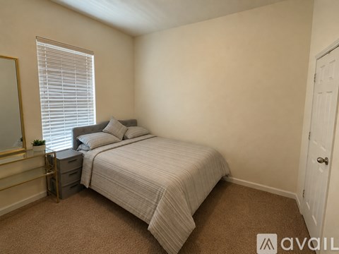 A bedroom with a bed, nightstand, and window with blinds.