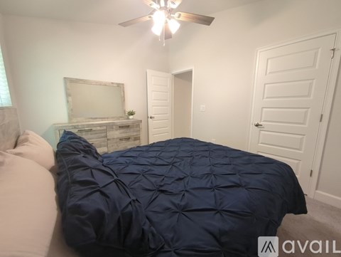 A bedroom with a bed covered in a blue comforter and a ceiling fan with lights.