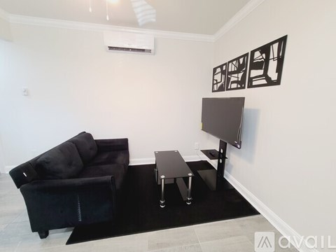 A black couch sits in a living room with a television and a black coffee table.