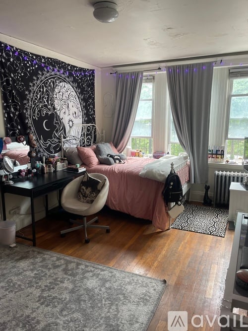A room with a desk and a bed with a pink blanket.