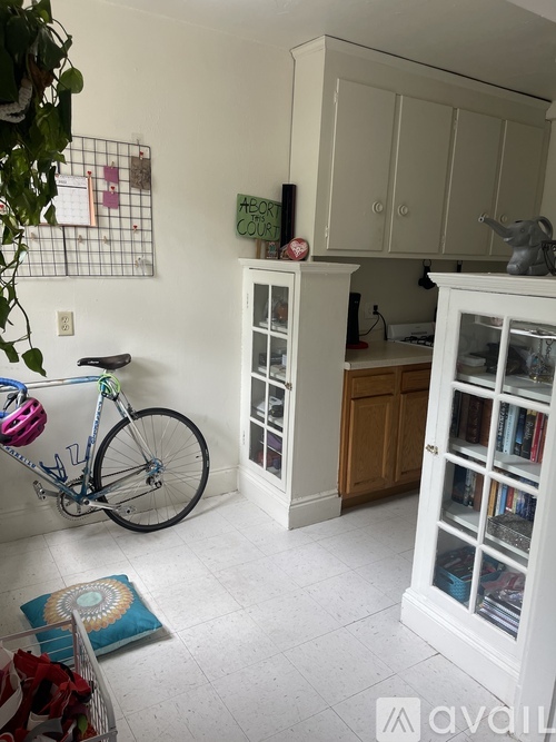 A bicycle is leaning against a wall in a room with a white floor and a white cabinet.