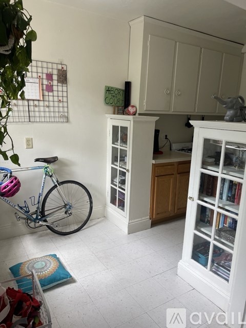 A bicycle is leaning against a wall in a room with a white floor and a white cabinet.