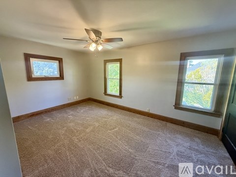 A room with a carpeted floor, a ceiling fan, and two windows.