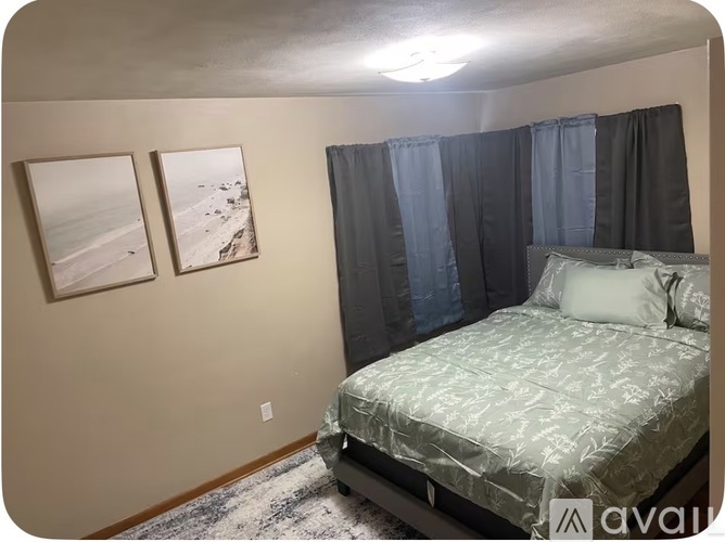 A bedroom with a bed, two pictures on the wall, and a rug on the floor.