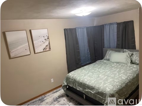 A bedroom with a bed, two pictures on the wall, and a rug on the floor.