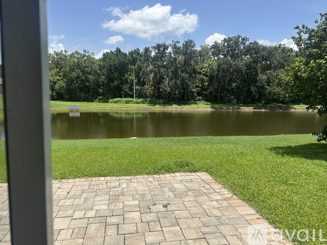 A paved walkway leads to a tranquil lake surrounded by lush greenery.