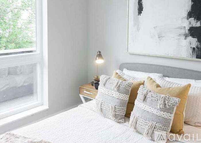 A bedroom with a bed, two pillows, a nightstand with a lamp, and a painting on the wall.