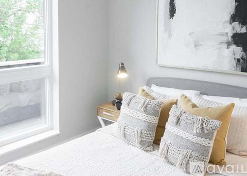 A bedroom with a bed, two pillows, a nightstand with a lamp, and a painting on the wall.