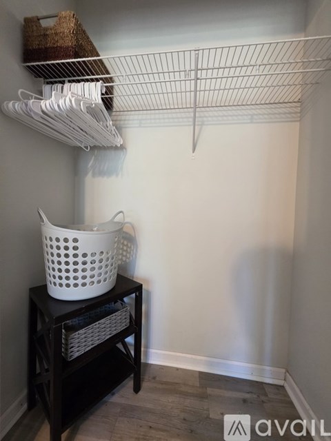 A white wire shelf with clothes hangers and a white laundry basket on a black table.