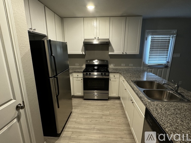 A kitchen with a black refrigerator, stainless steel oven, and white cabinets.