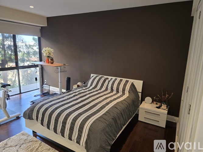A bedroom with a bed, nightstand, and a window with a view of trees.