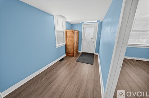 A room with blue walls and wooden flooring, featuring a white door and a brown door.