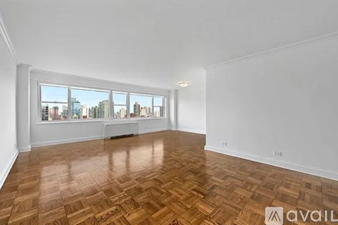 A room with wooden flooring and a large window overlooking a cityscape.