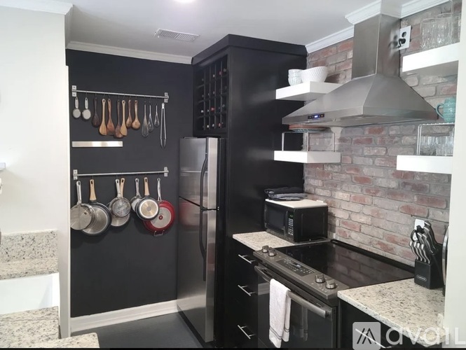 A kitchen with a black refrigerator and a brick wall.