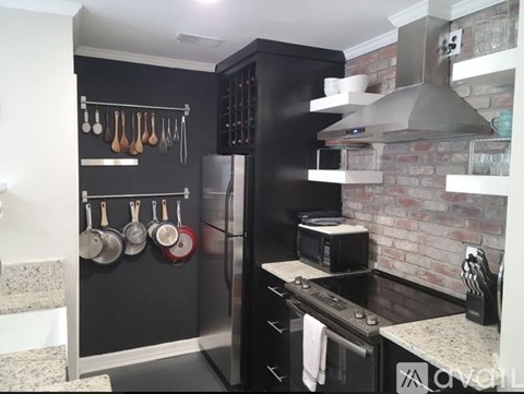 A kitchen with a black refrigerator and a brick wall.