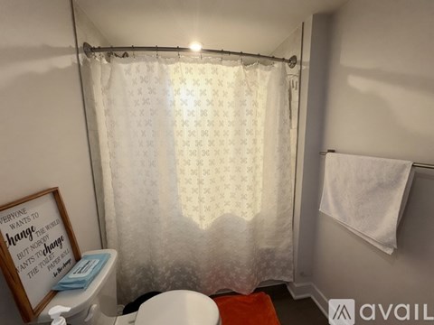 A bathroom with a toilet, a shower curtain, and a towel hanging on the wall.