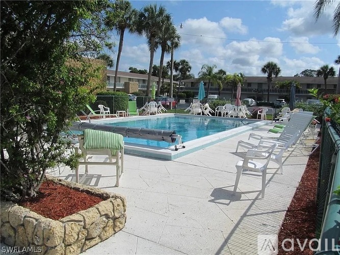 A pool surrounded by chairs and trees.