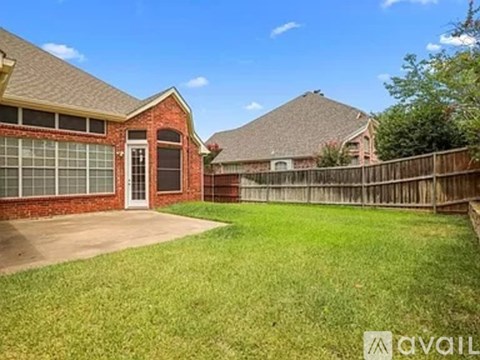 A house with a red brick exterior and a white door is surrounded by a wooden fence and has a green lawn.